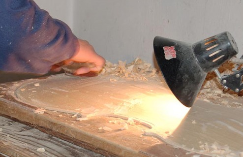 A maker shapes the arching of a violin plate under a lamp.
