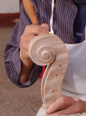 A maker carves the spiral of a cello scroll.