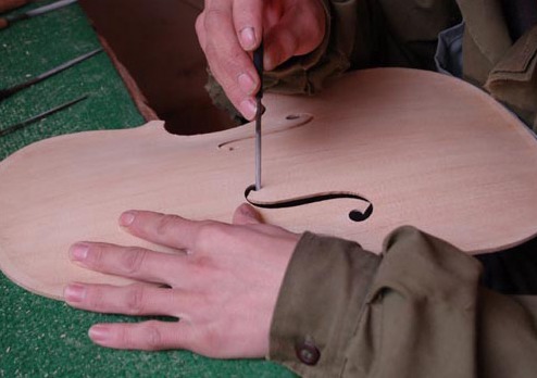 A maker cuts an f-hole into a violin front with a small knife.