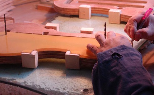 A maker marks the outline of a violin onto the blocks of a mould.