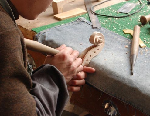 A maker carves the pegbox of a violin scroll with a gouge.