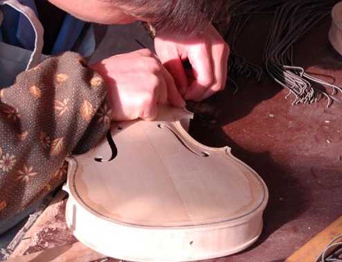 A maker inserts purfling into the channel around the edge of a white violin body.